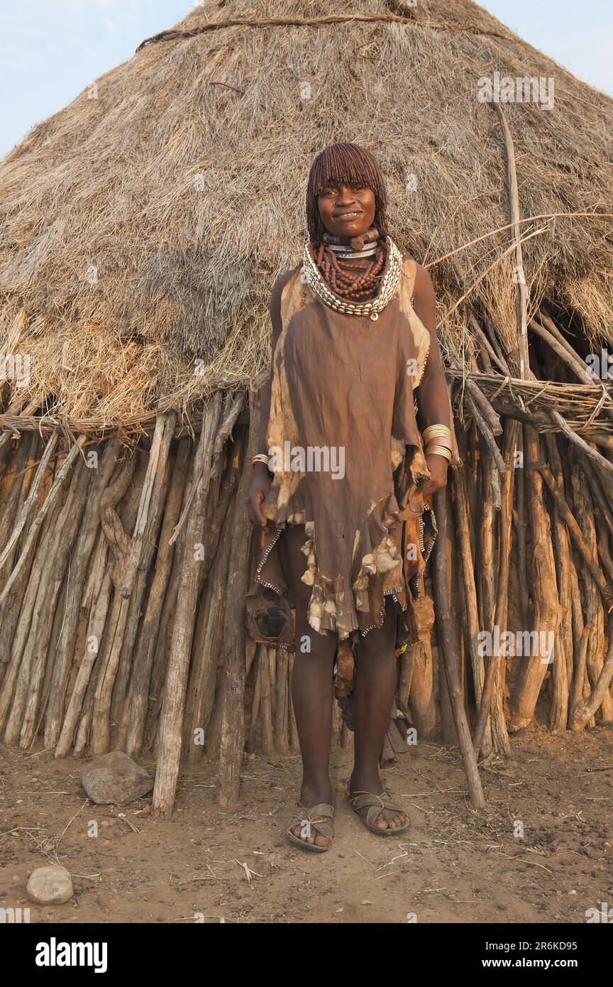 Pregnant Hamar woman, necklace made of cowrie shells, in front of wooden hut, Hamar tribe, Omo valley, southern Ethiopia, Hamar Stock Photo