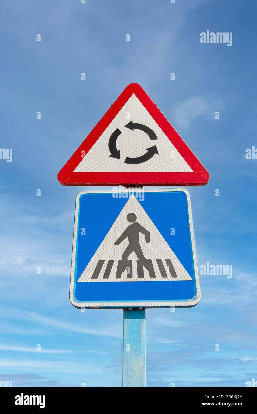 Roundabout and pedestrian crossing road signs against a blue sky