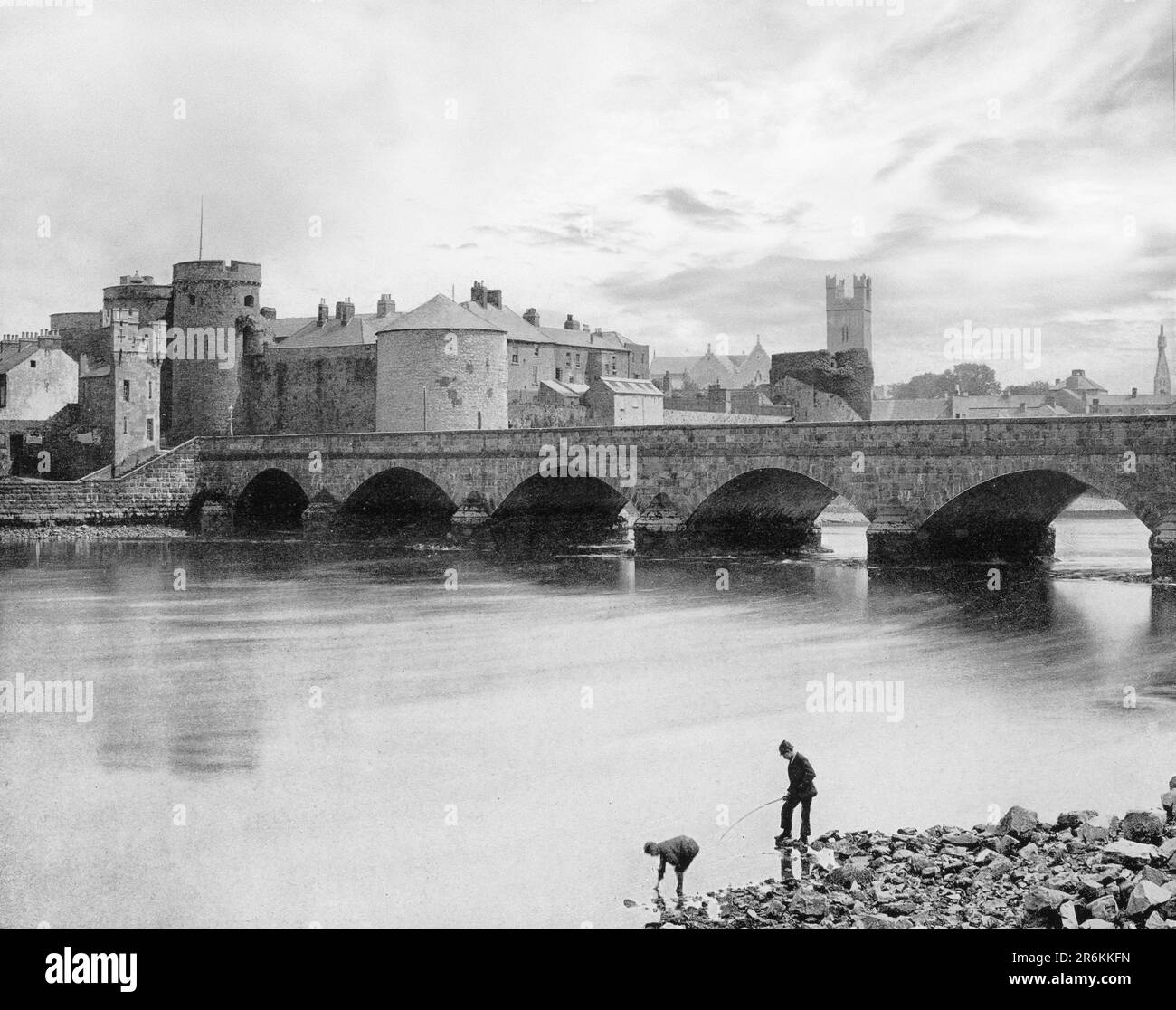 A late 19th century view of people fishing beside the  Thomond Bridge built in 1836 and beyond is 13th-century King John's Castle, aka Limerick Castle, Ireland. Although the site dates back to 922 when the Vikings lived on the Island, the castle itself was built on the orders of King John in 1200. One of the best preserved Norman castles in Europe, the walls, towers and fortifications remain today. Stock Photo