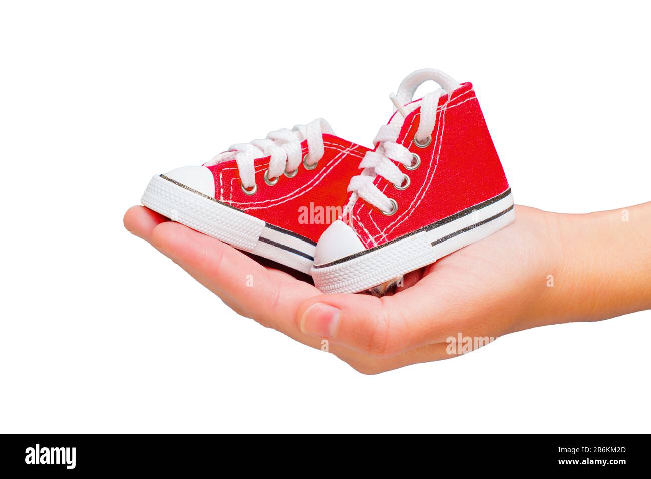 Tiny red high-top canvas shoes resting on a hand palm isolated on white with copy space. Stylish toddlers footwear concept. Stock Photo