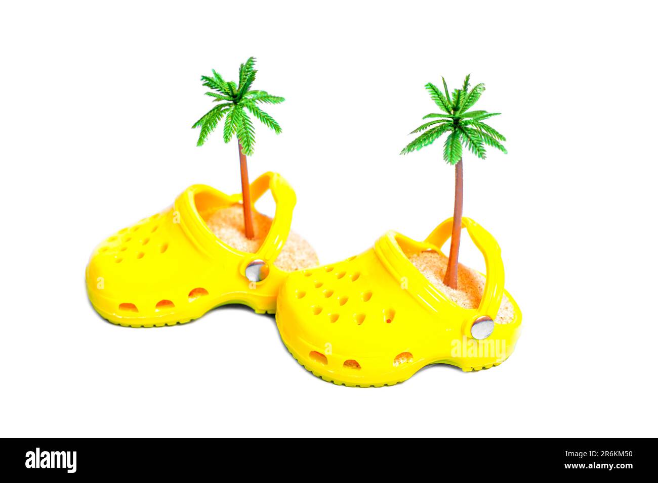 Miniature yellow clogs with sand and toy palm trees isolated on white