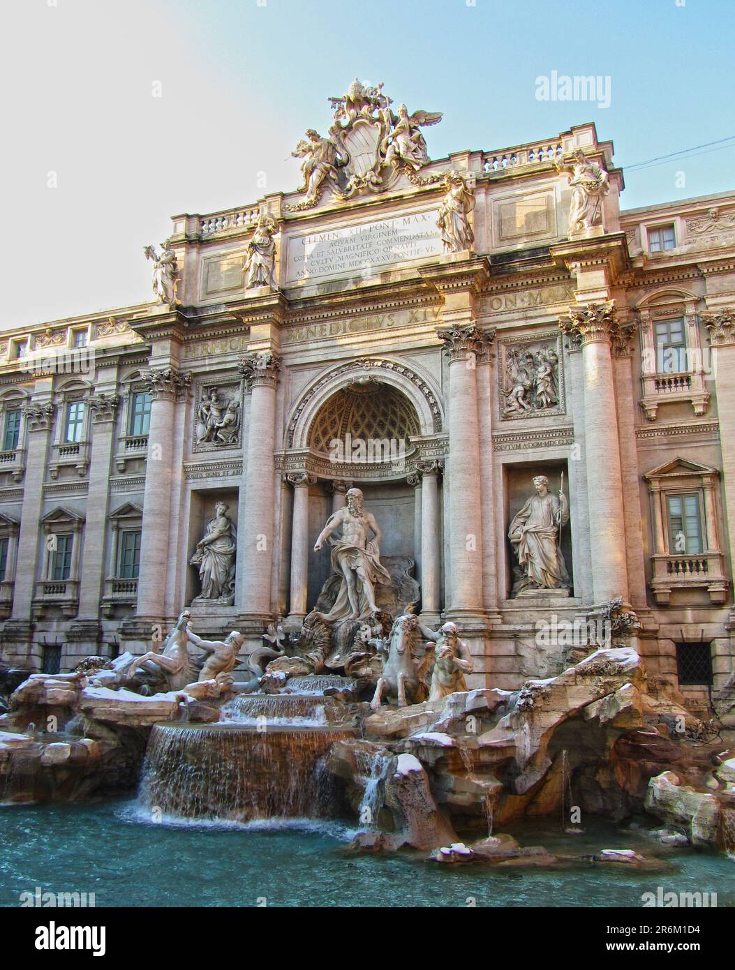 A majestic building with intricate stonework and statuesque figures in the foreground, set against a tranquil backdrop of a flowing fountain Stock Photo