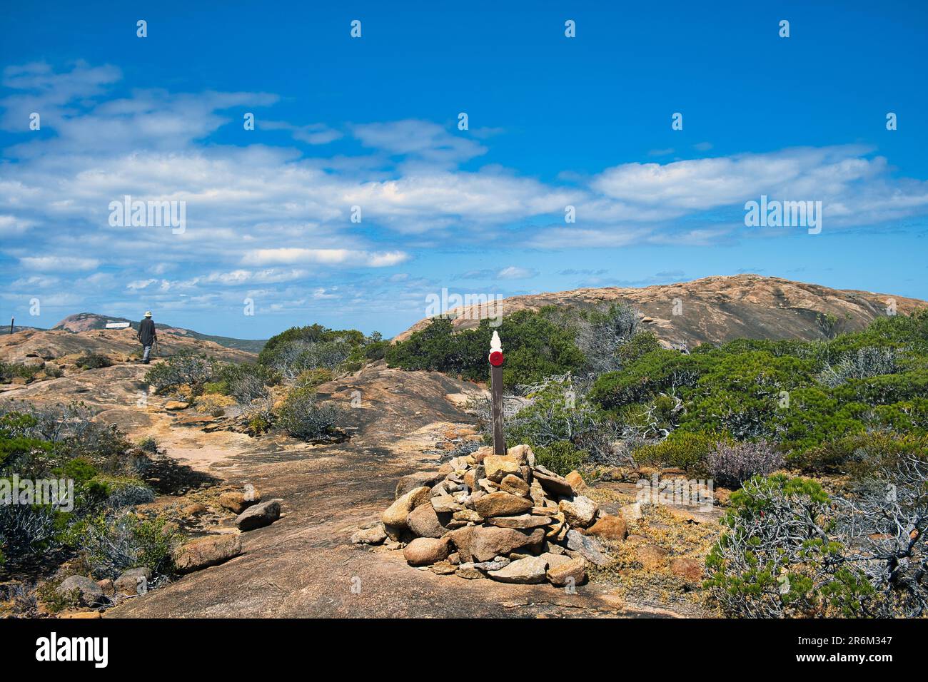 Trail marker, hiker, low coastal vegetation and lichen-covered granite hills along the Coastal Trail in Cape Le Grand National Park, Western Australia Stock Photo
