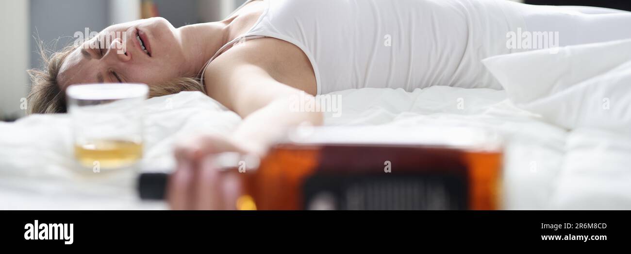 Drunk woman is sleeping on bed with bottle of alcohol Stock Photo