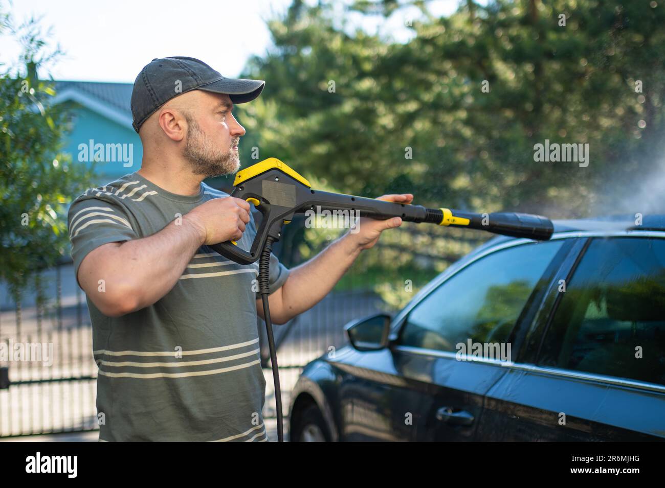 Young man using a water gun to wash his car. Male driver washing a car