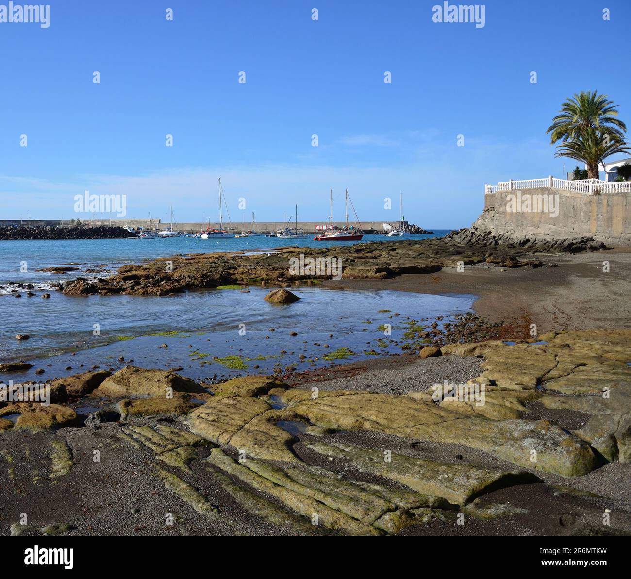 Beach at low tide in foreground, port in the background and blue sky, coast of Arguineguin, Gran Canaria, Canary Islands Stock Photo
