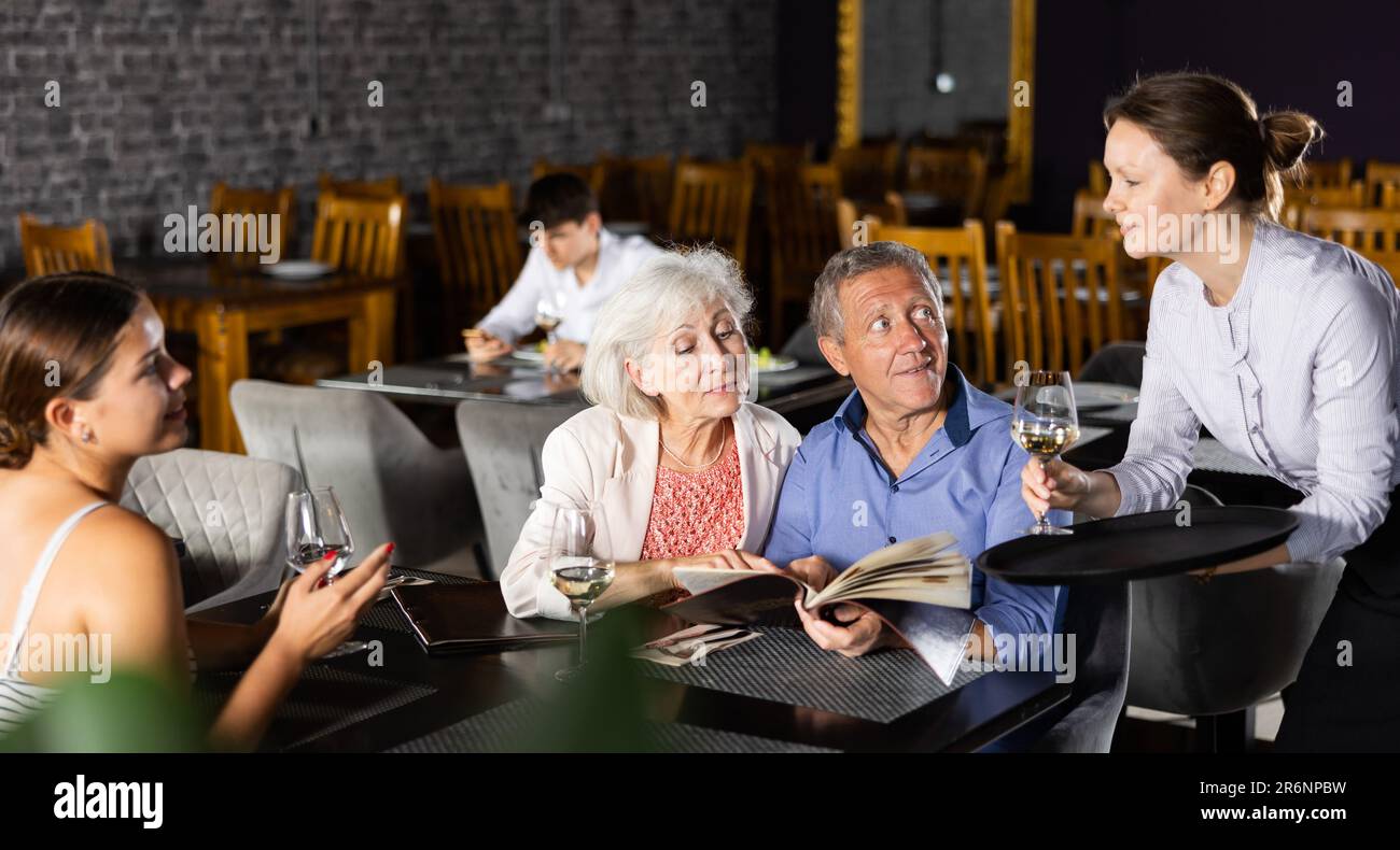 Waitress serving wine to guests perusing menu in restaurant Stock Photo ...
