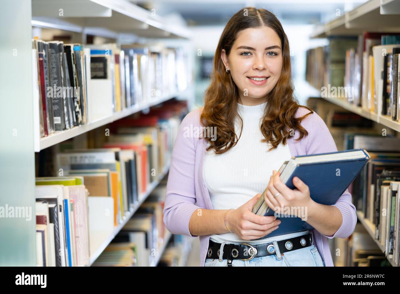 Portrait of woman holding books at library Stock Photo - Alamy