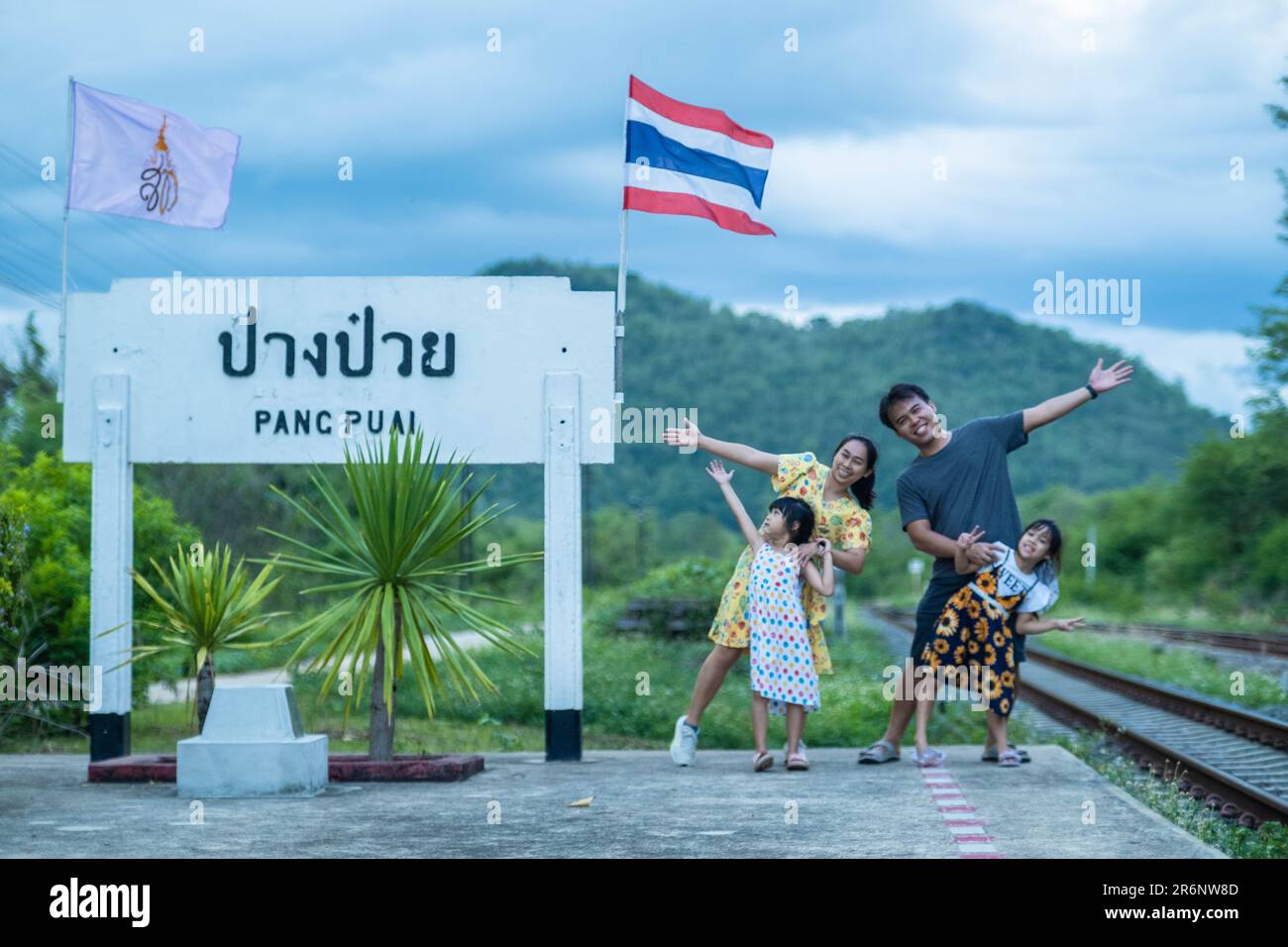 8 June 2023: Lampang, Thailand - Happy family taking pictures together at Pang Puai Railway Station against a background of green mountains and trees. Stock Photo