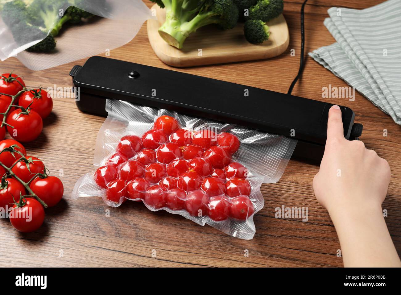 Woman packing cherry tomatoes using vacuum sealer on wooden table