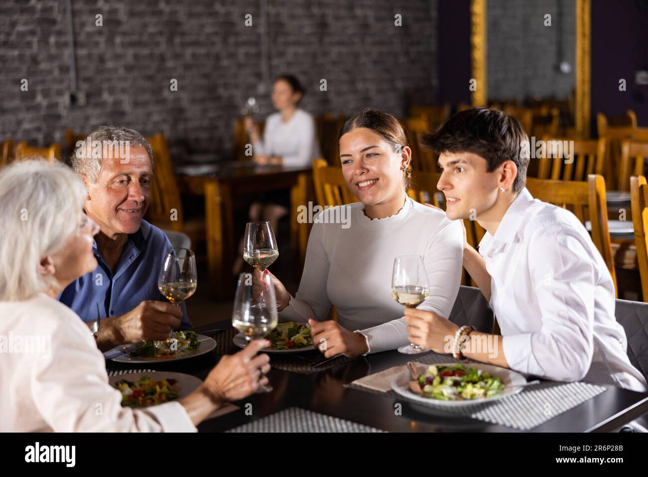 Young family and elderly couple of spouses eating in cafe celebrating event and communicating Stock Photo
