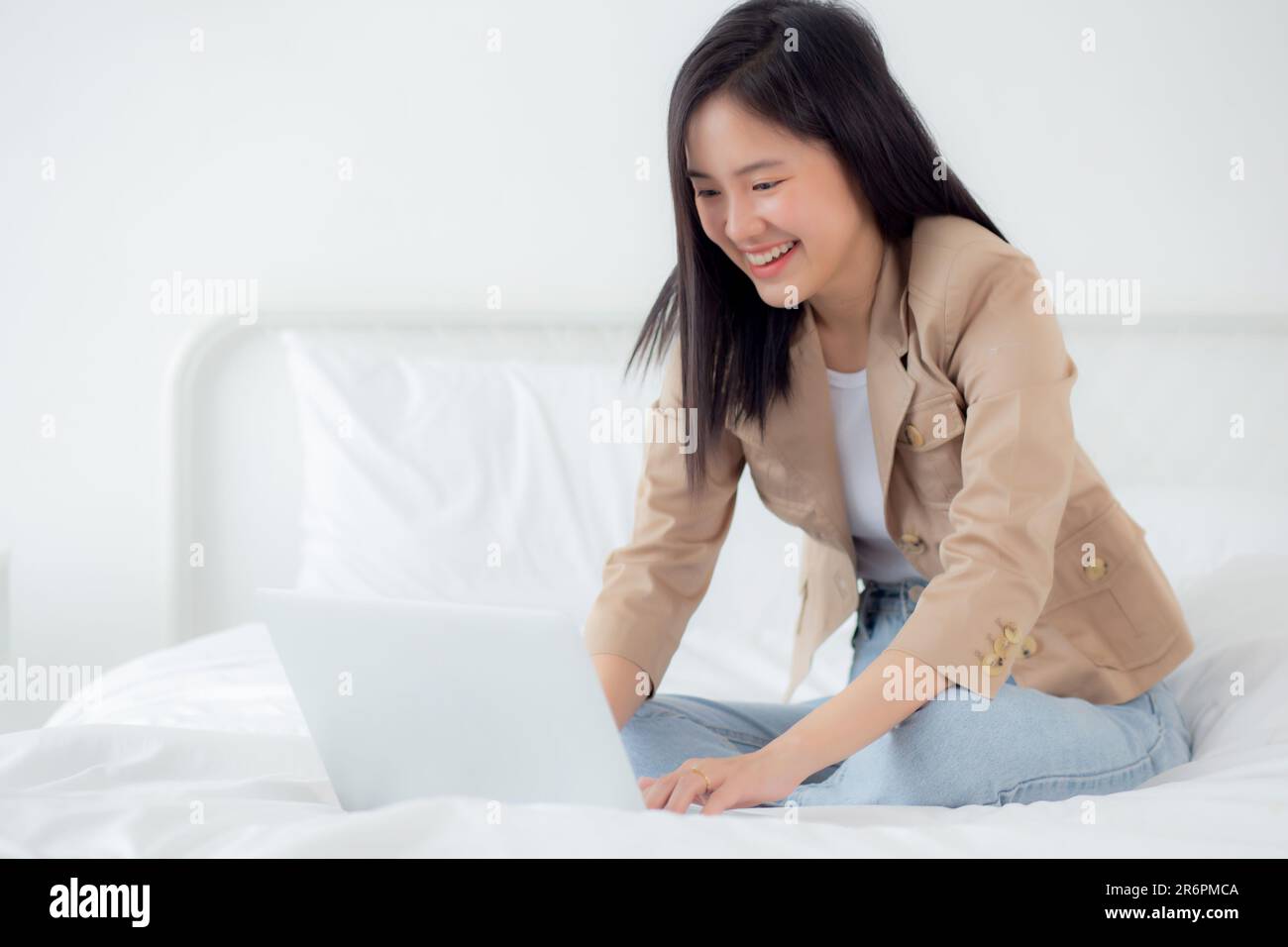 Beautiful young asian woman sitting on bed using laptop computer ...