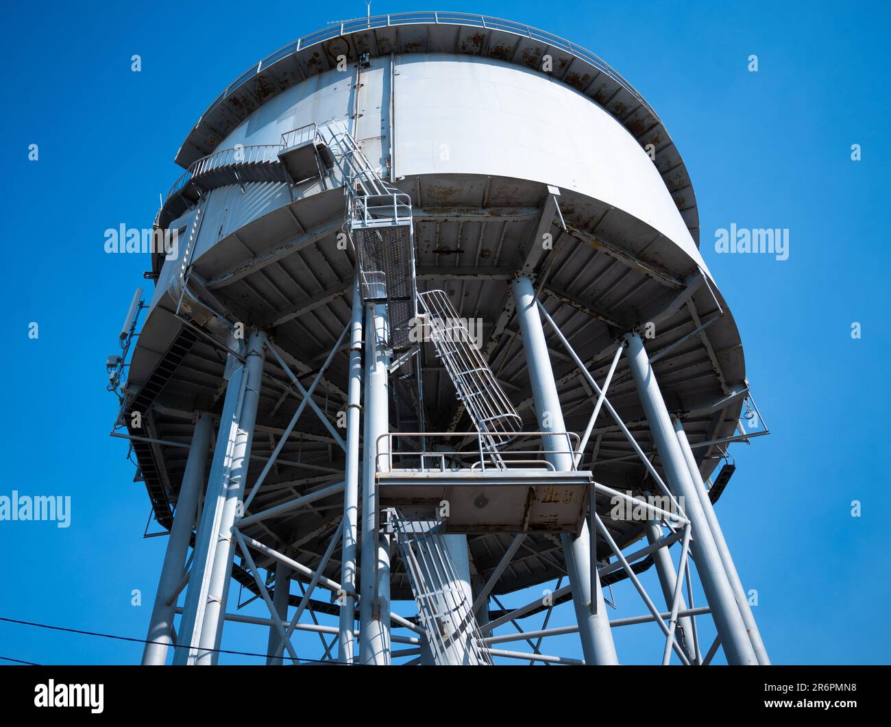 A low angled photograph of a grey colored water tower in Nightcliff, Darwin. Structural engineering supports a full water tank. Stock Photo