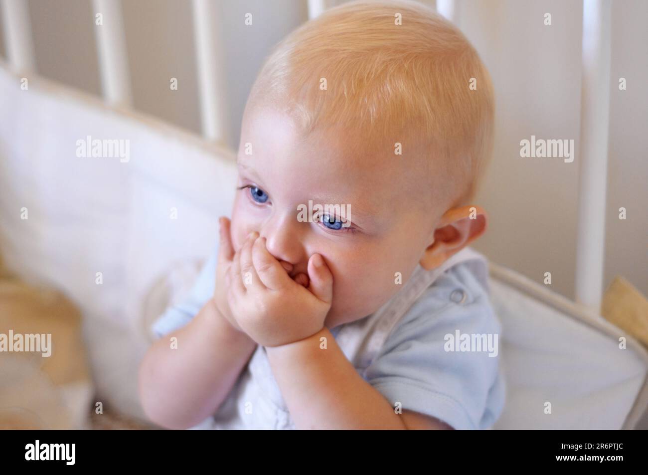 Happy, face and toddler standing in crib, bedroom or excited baby boy with hands on teething mouth for morning surprise of mistake. Kid sitting in cot Stock Photo