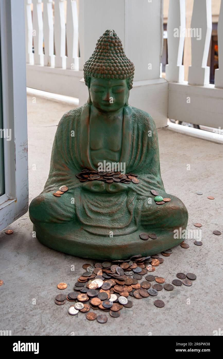 Buddha statue on the floor being used as a doorstop with coins in its lap and on the floor. Stock Photo