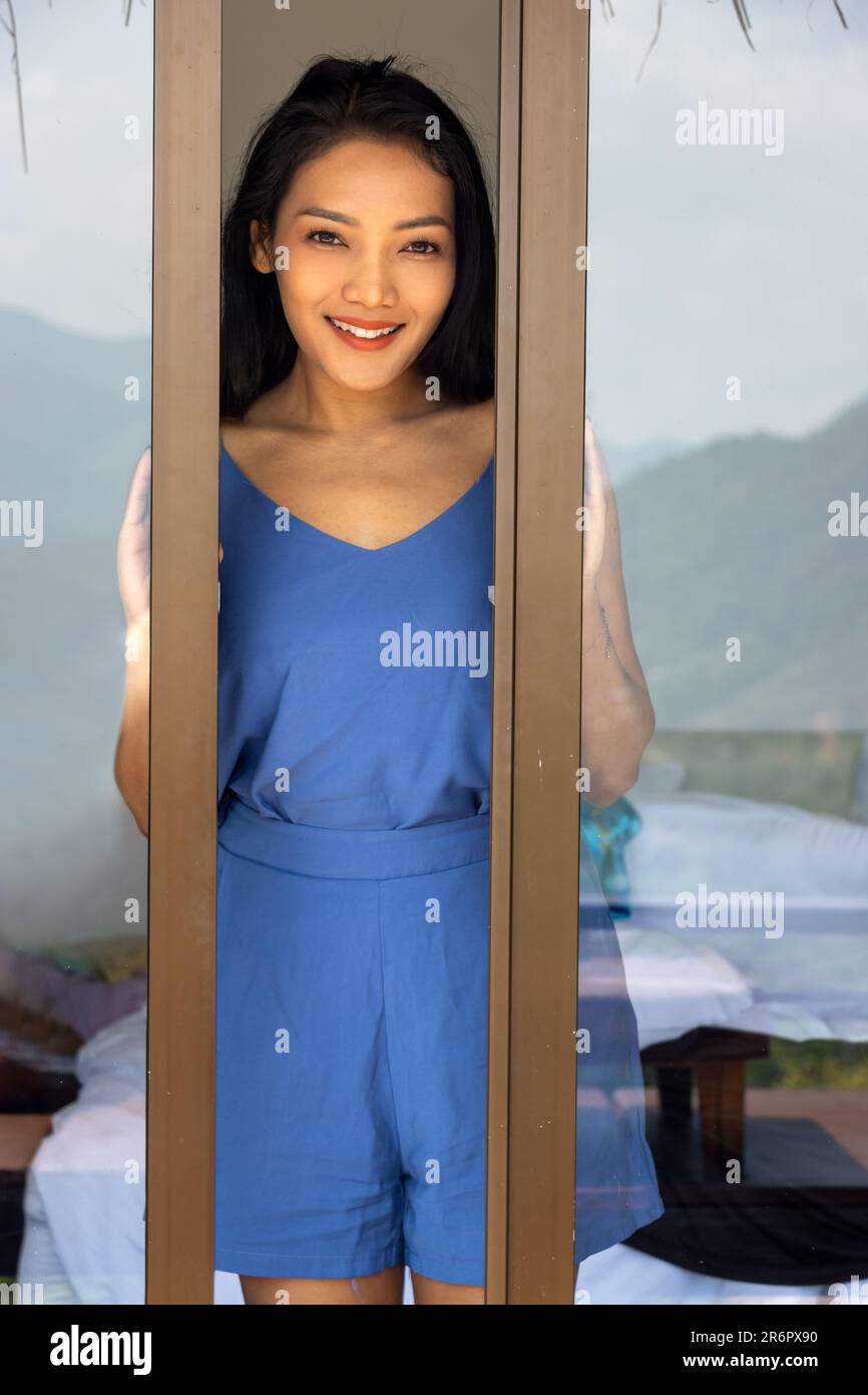 A young woman opens the balcony door and looks to camera Stock Photo