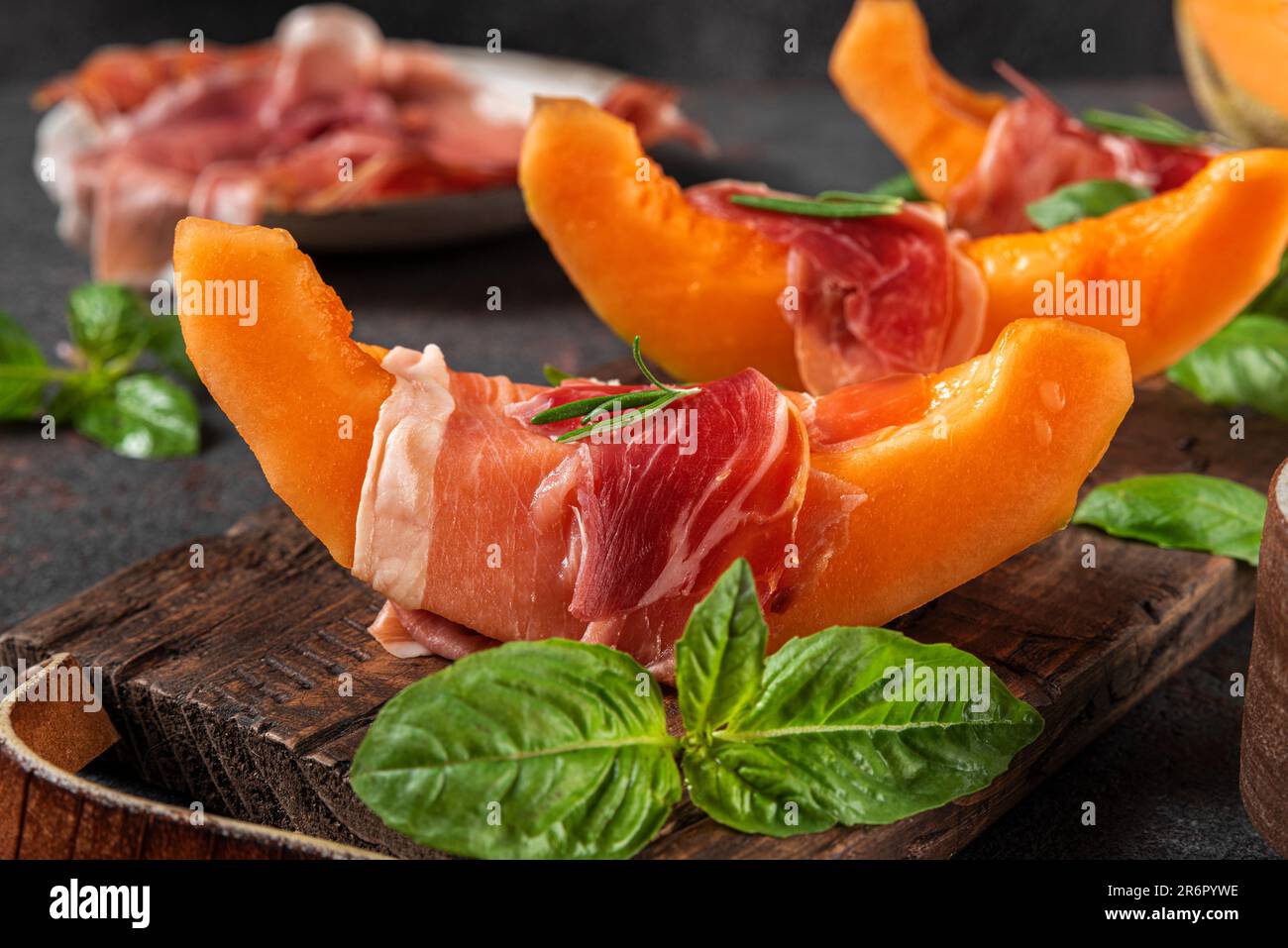 Fresh melon cantaloupe with prosciutto ham and basil on black ...