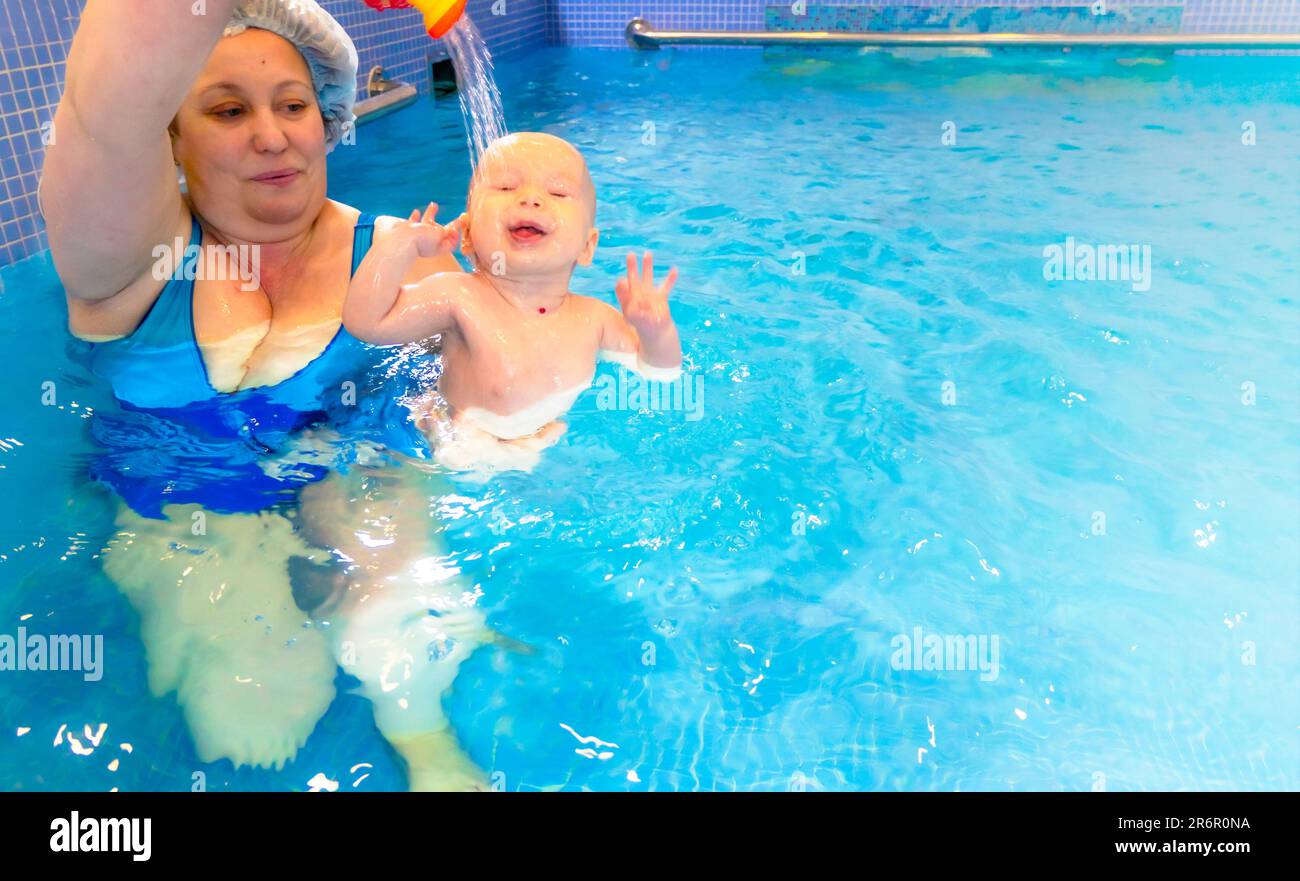 Adorable baby girl enjoying swimming in a pool with her mother early