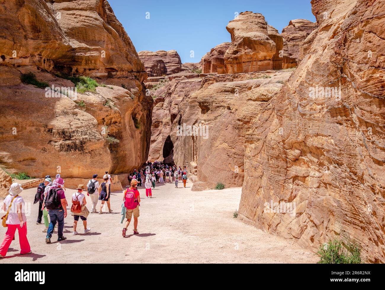 Tourists walk towards the Siq, the narrow gorge that is the main entrance leading to the Treasury and the ancient city of Petra, in Jordan. Stock Photo