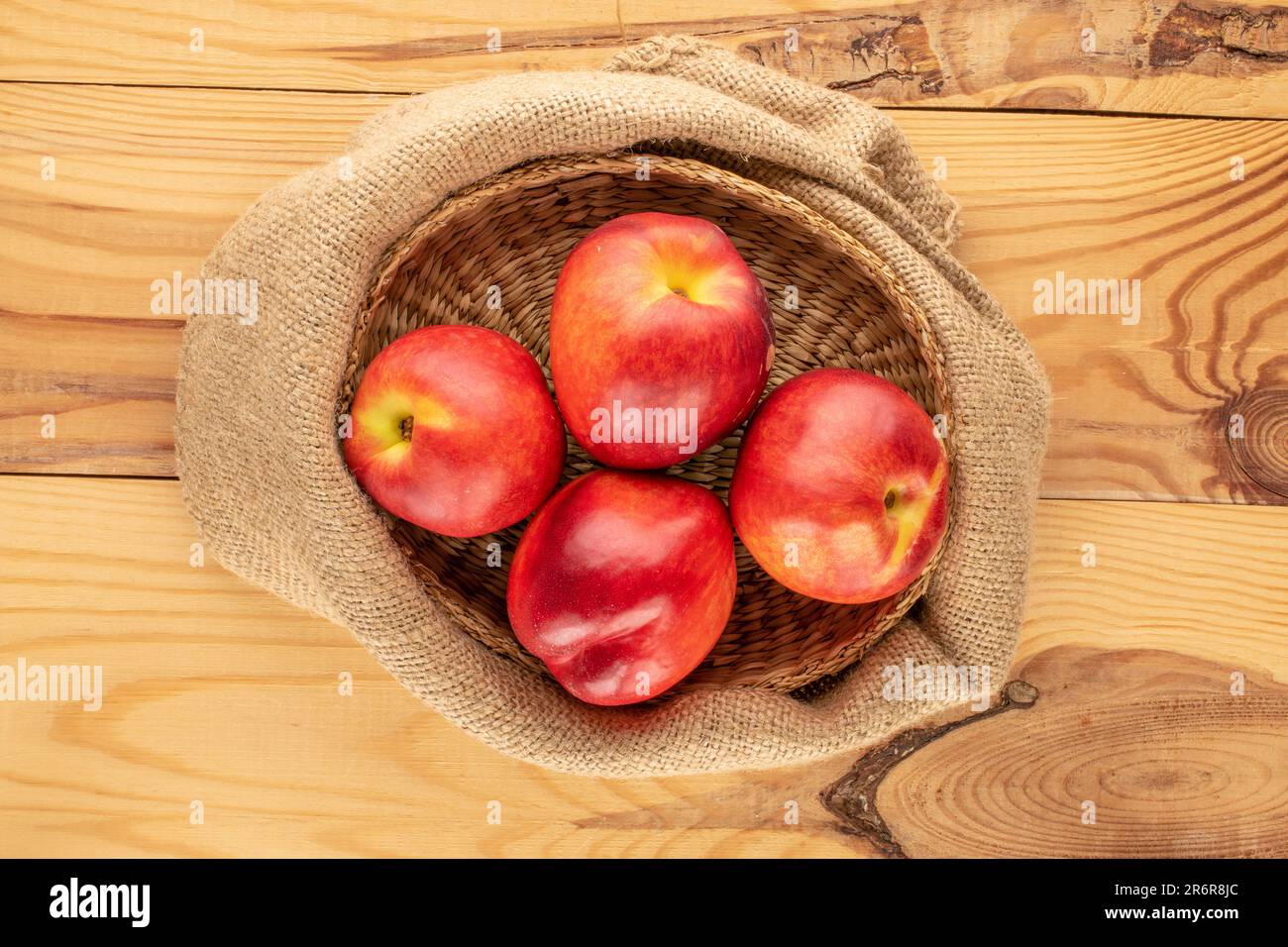 Several ripe nectarines with a jute bag on a wooden table, macro, top view. Stock Photo