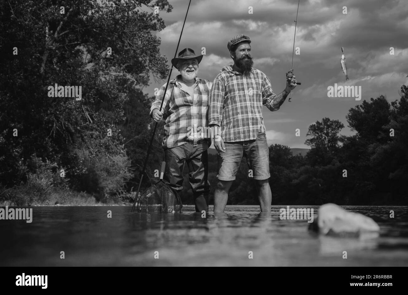 Happy father and son together fishing in summer day under beautiful sky on the river. Fly fishing. Fly fisherman using fly fishing rod in beautiful Stock Photo