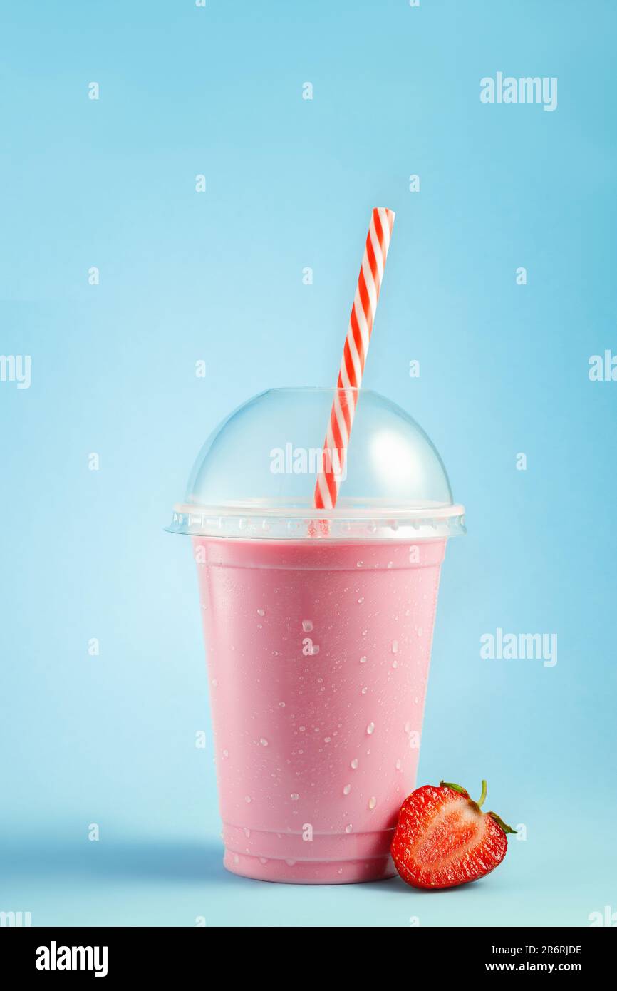 strawberry milkshake in disposable plastic glass with straw on blue