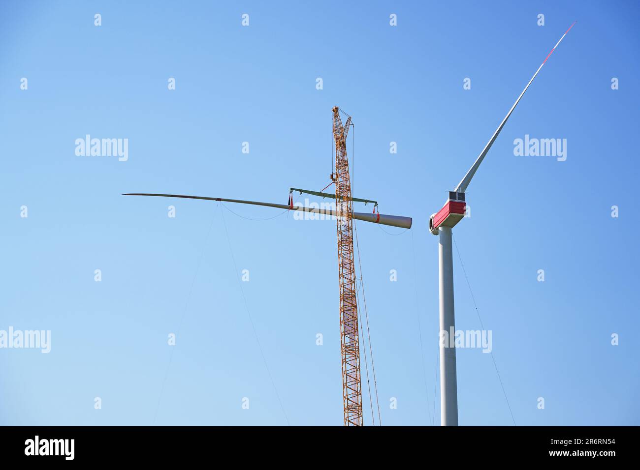 Installing a wind turbine, crane is lifting the second blade to install it to the rotor hub on the tower, heavy industry for electricity, renewable en Stock Photo