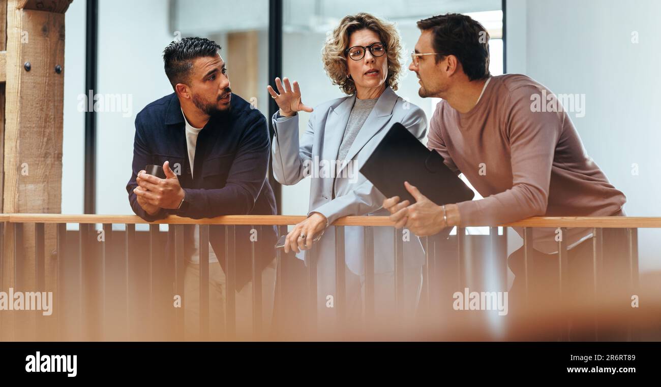 Interior designers discuss with each other in an office. Three business people talking while standing on an interior balcony. Group of creative busine Stock Photo