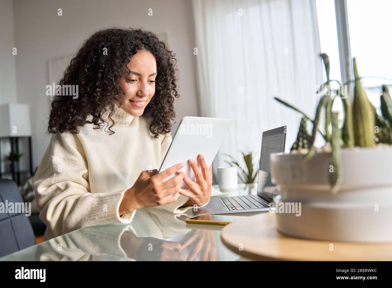 Young happy latin woman using digital tablet at home looking at tab. Stock Photo