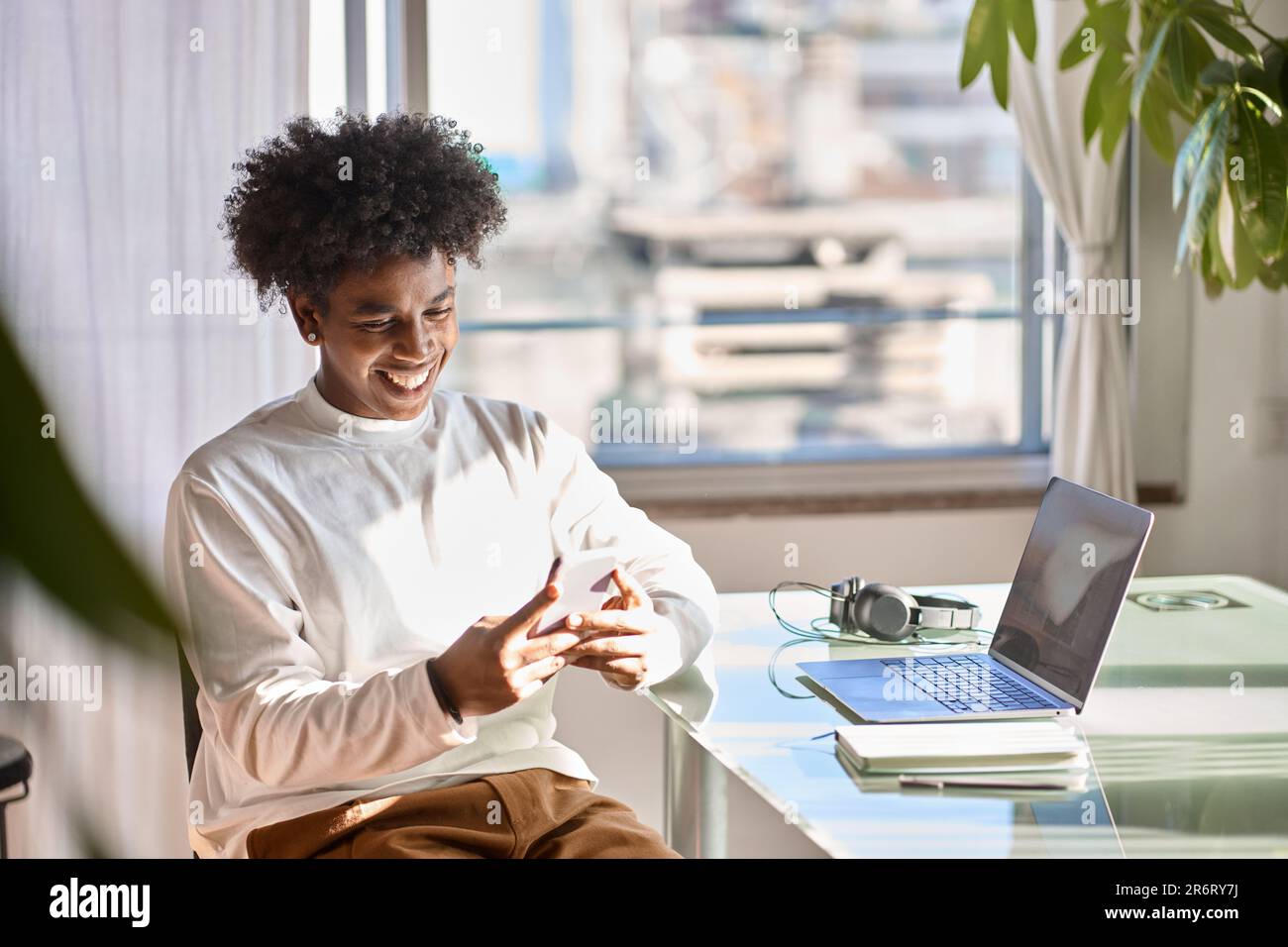 Smiling young African American guy using mobile phone at home. Stock Photo