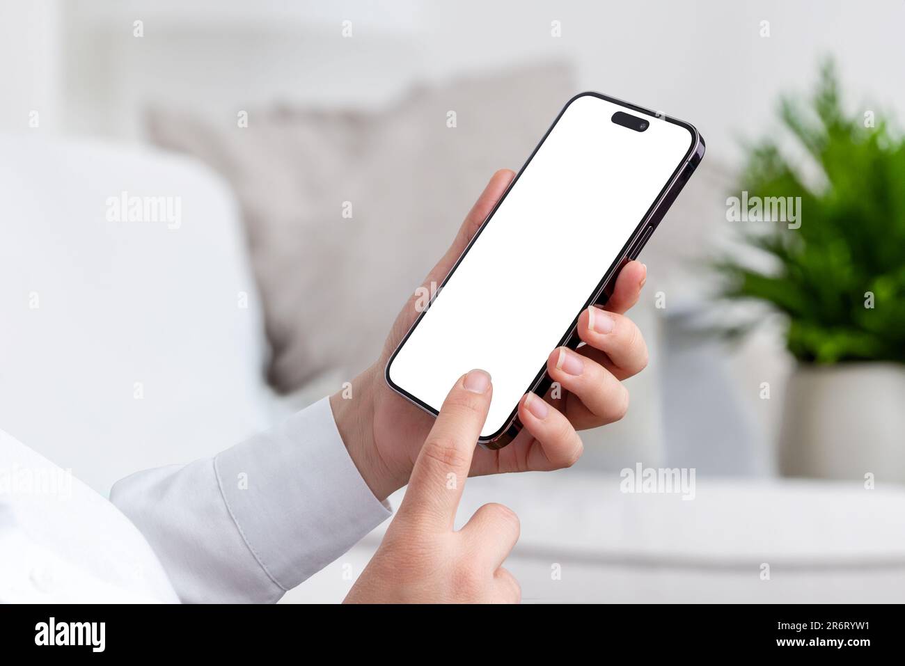 Woman holds modern smartphone, dressed in a white shirt, standing in living room. Isolated mobile screen for app or web page presentation Stock Photo