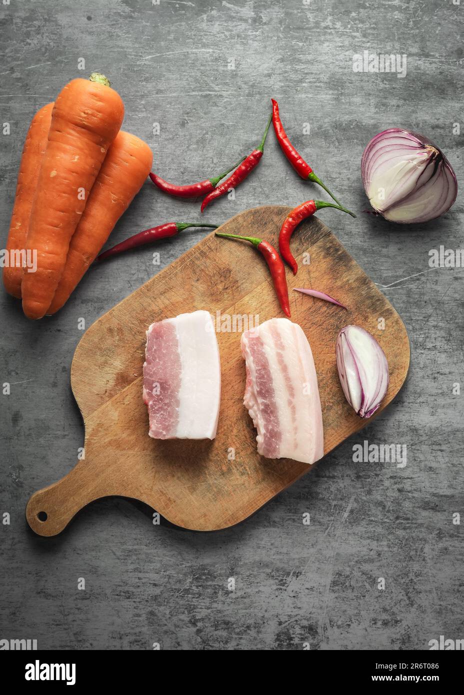 Carrots, chili peppers, pork belly, and onions placed on a table board. Stock Photo