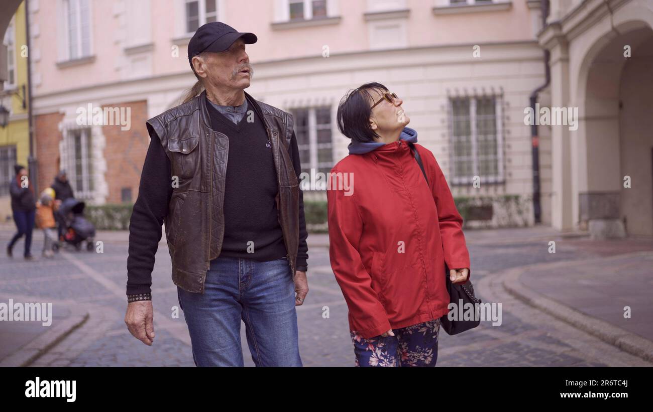 Elderly couple of tourists are walking through the historical center seeing  the sights and looks at up in an old European city. Palace Square, Warsaw Stock Photo