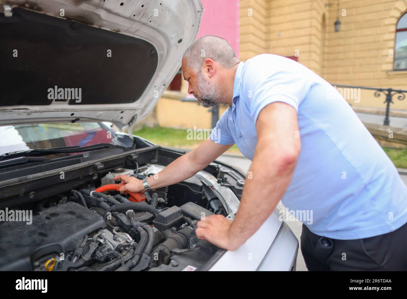 A bearded man leaned over the open hood of a black car with a