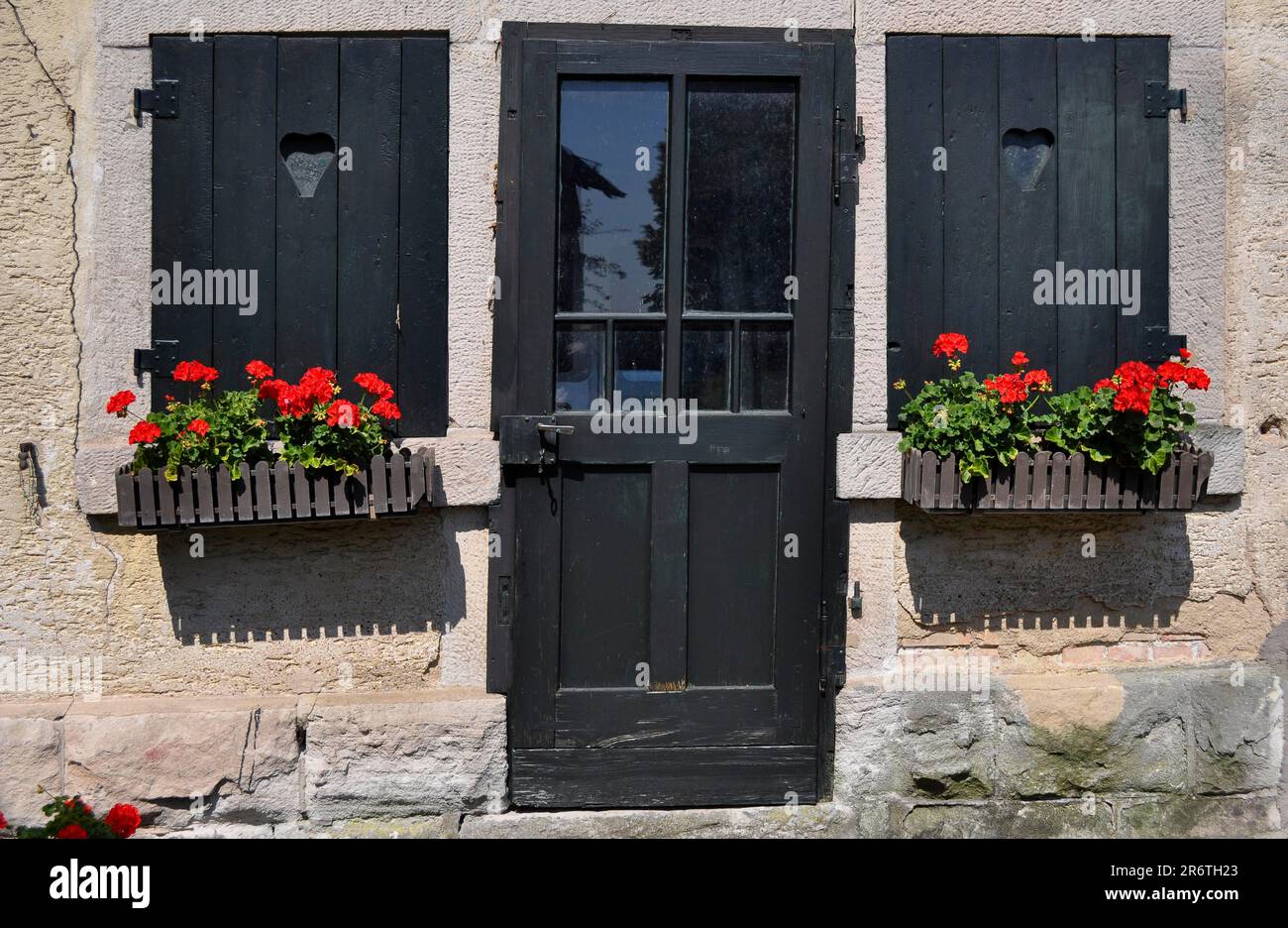 Wooden door with wooden shutters, flowers on the window outside, red geraniums in the box, Pelargonium Stock Photo