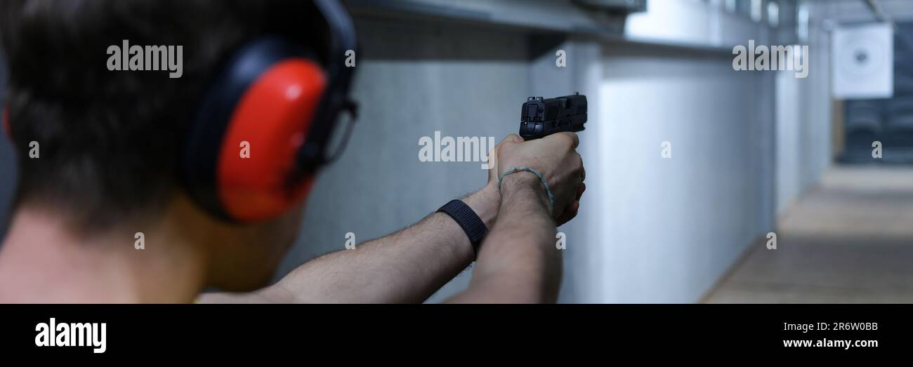 Male shooter in headphones aiming pistol at target in shooting range