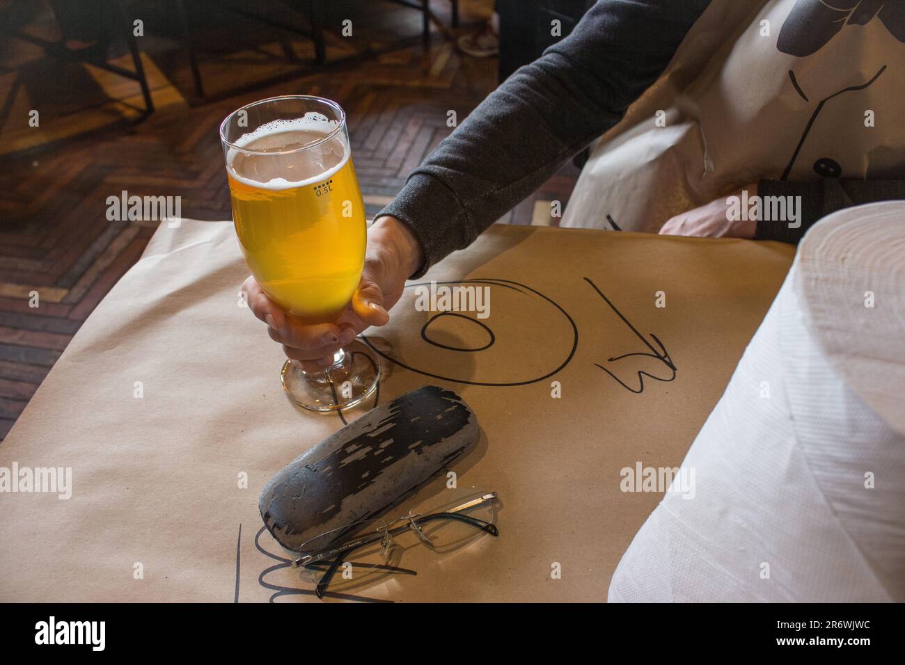 Hand holding glass of beer in restaurant. Beer and eyeglasses on the table. After work drinks. Man in pub with beer. Alcohol drinks. Cheers concept. Stock Photo