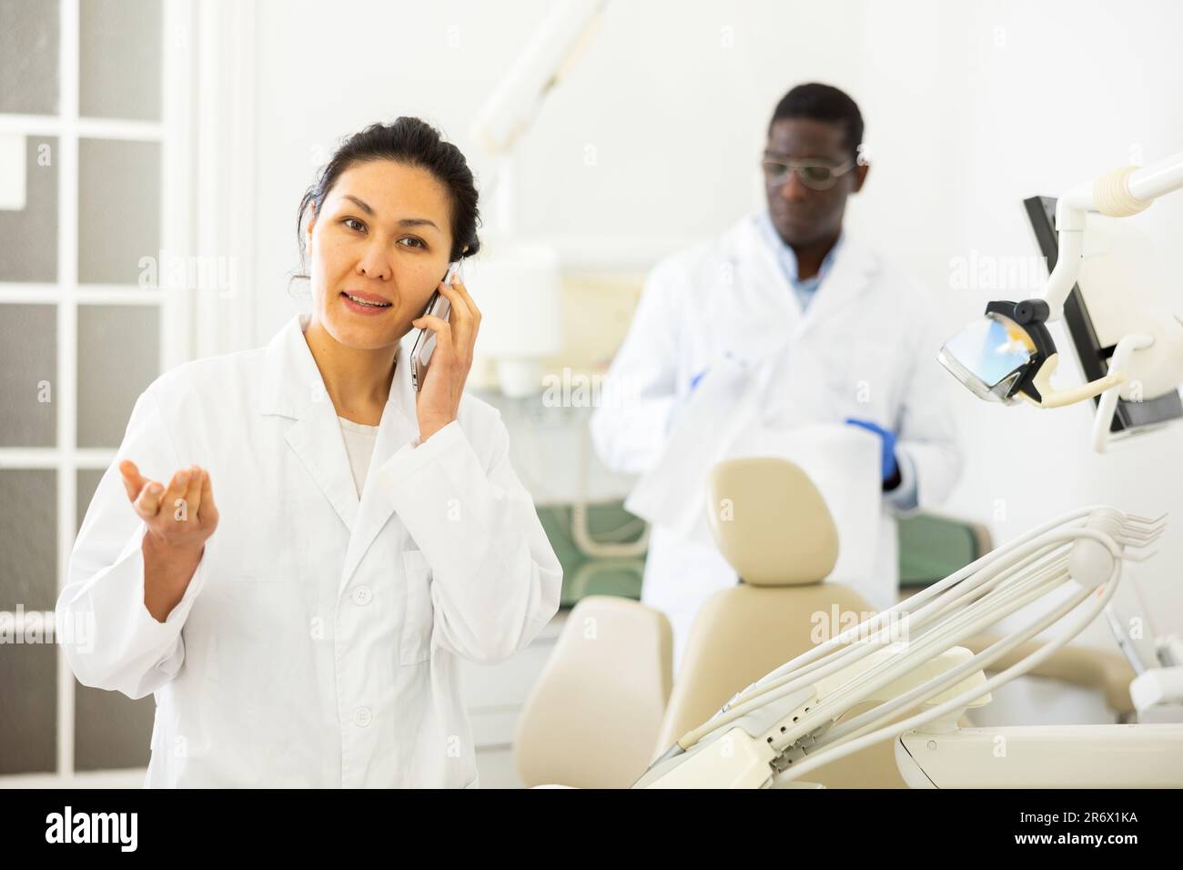 Portrait of friendly female dentist with a mobile phone. Invites