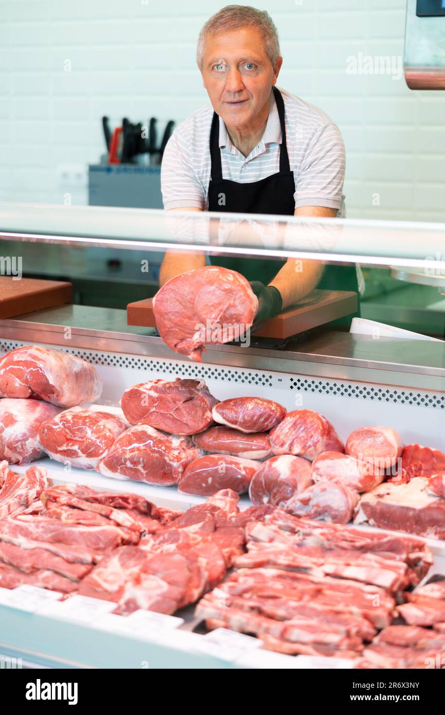 Male farmer of meat products in butcher shop offers to buy fresh beef