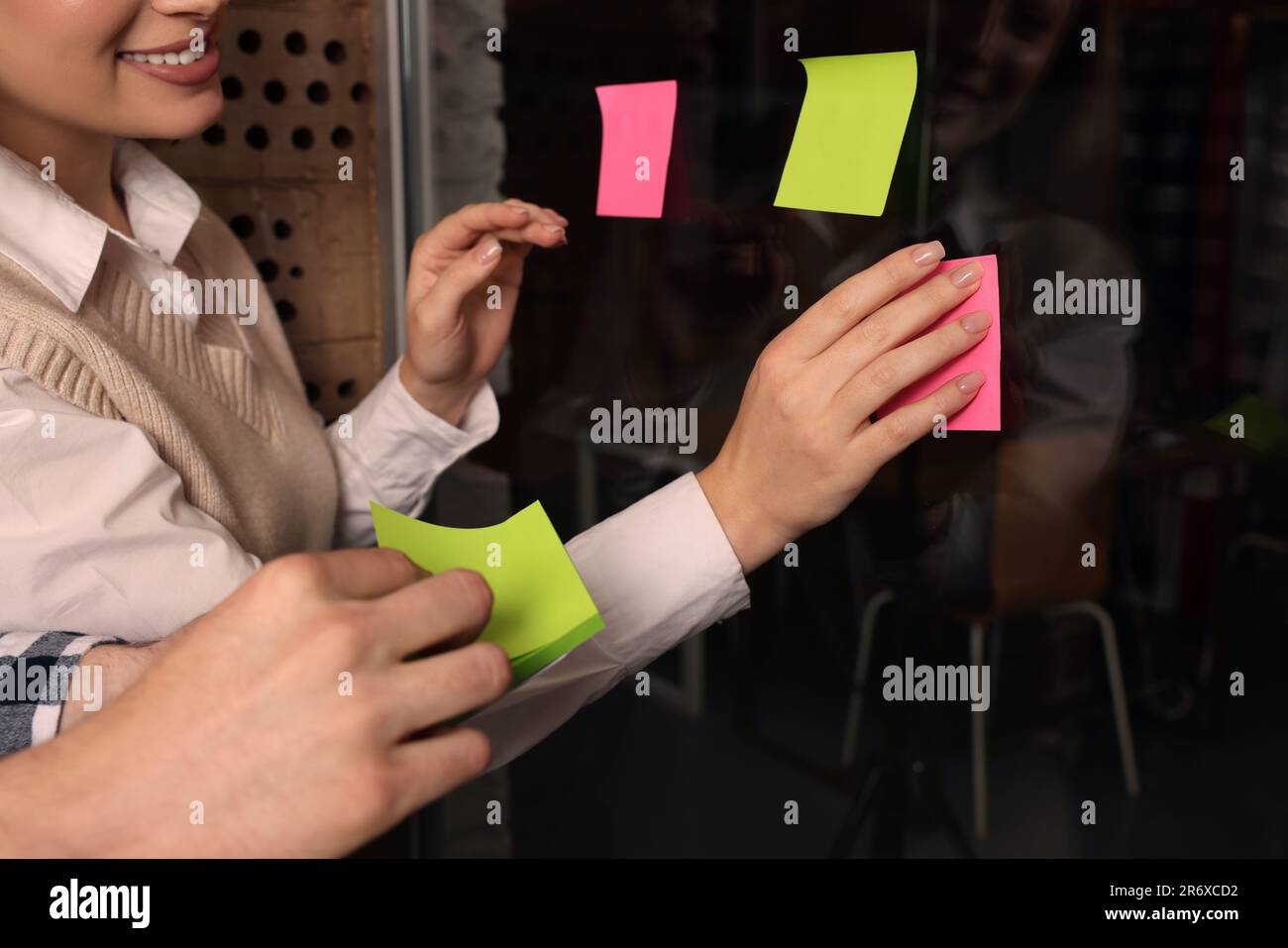 Employees putting colorful sticky notes on glass door in office, closeup. Team work motivation Stock Photo