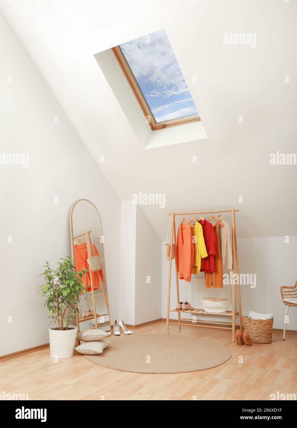 Stylish clothes rack, mirror and wicker chair in attic room. Interior