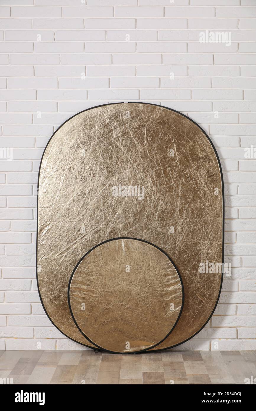 Professional golden reflectors in room near white brick wall