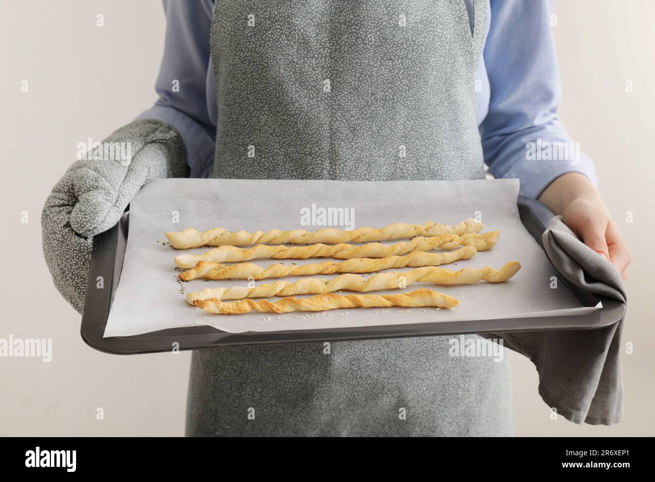 Woman holding baking sheet with homemade breadsticks on light grey