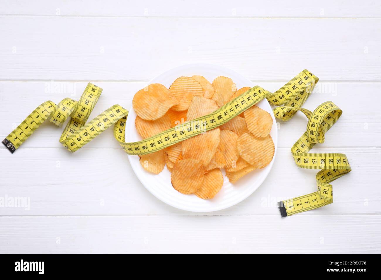 Plate with potato chips and measuring tape on white wooden table, flat
