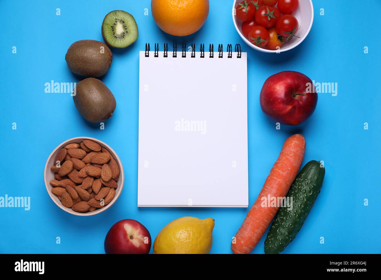 Notebook, almonds, fresh fruits and vegetables on light blue background, flat lay. Low glycemic
