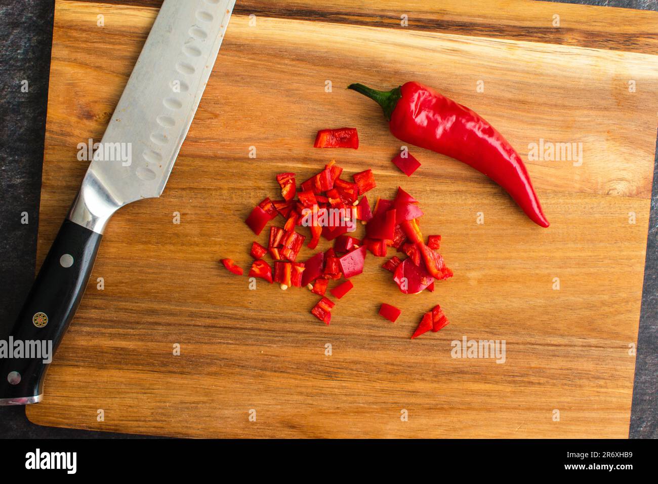 Chopped Red Chili Pepper on a Wooden Cutting Board: Whole red chile pepper next to a diced chile pepper and chef's knife Stock Photo