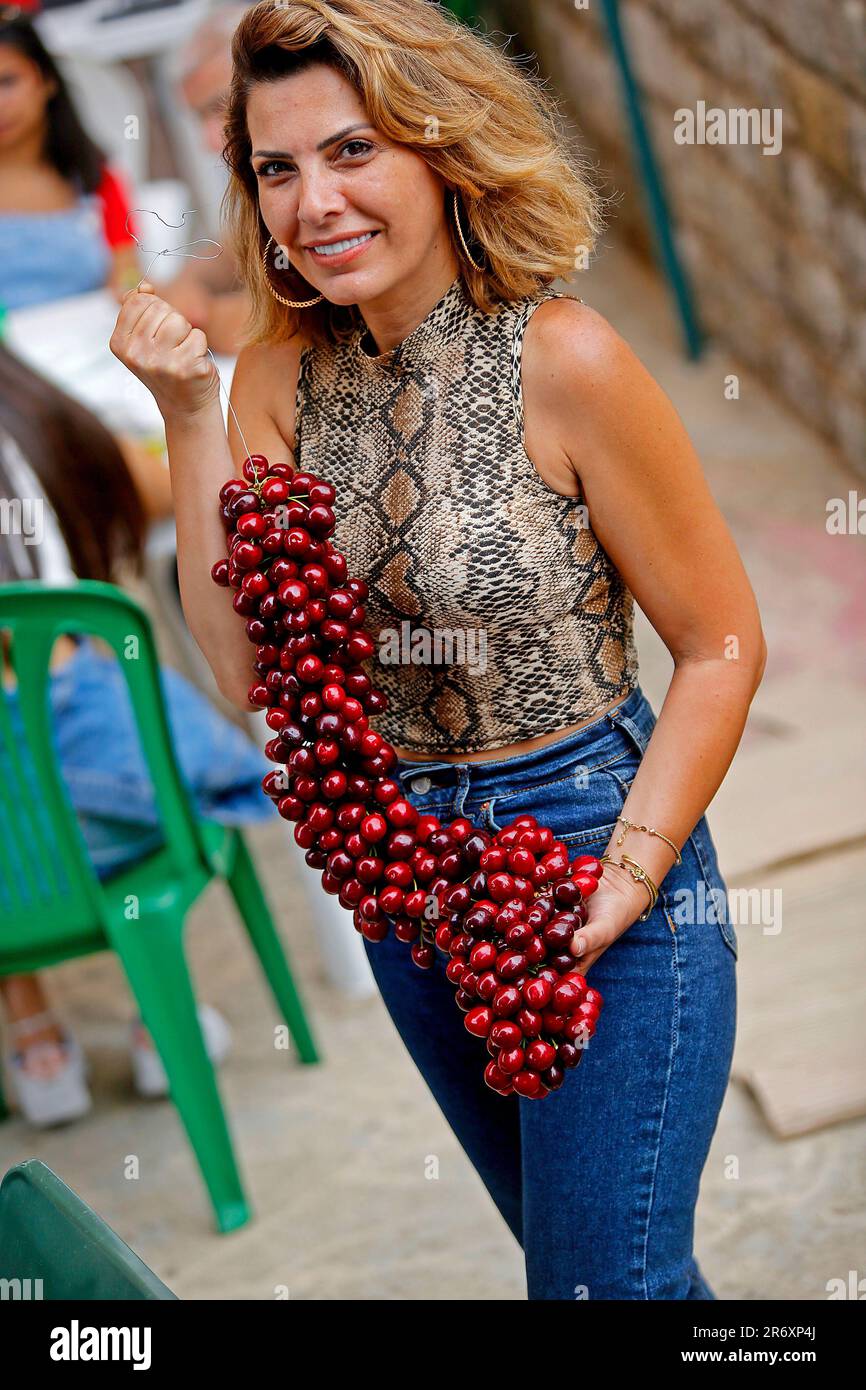 Hammana, Lebanon. 11th June, 2023. A woman poses for photos with a cluster of cherries on Cherry