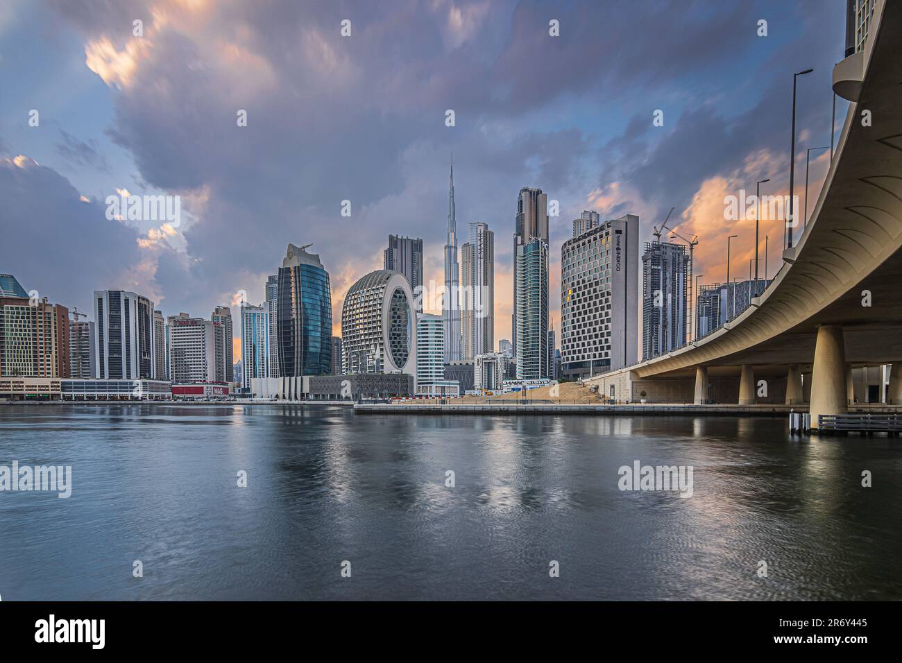 Sunset with a cloudy sky over the financial district of Dubai. City skyline in business center with office buildings and skyscrapers by Burj Khalifa Stock Photo