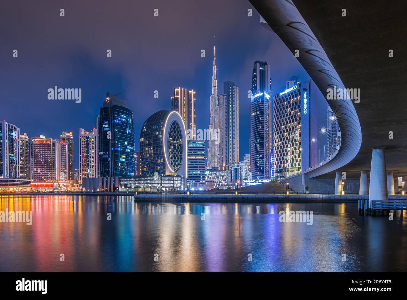 Dubai at night. City skyline in United Arab Emirates. Skyscrapers illuminated at the blue hour with a curved course of a bridge. Reflections on water Stock Photo