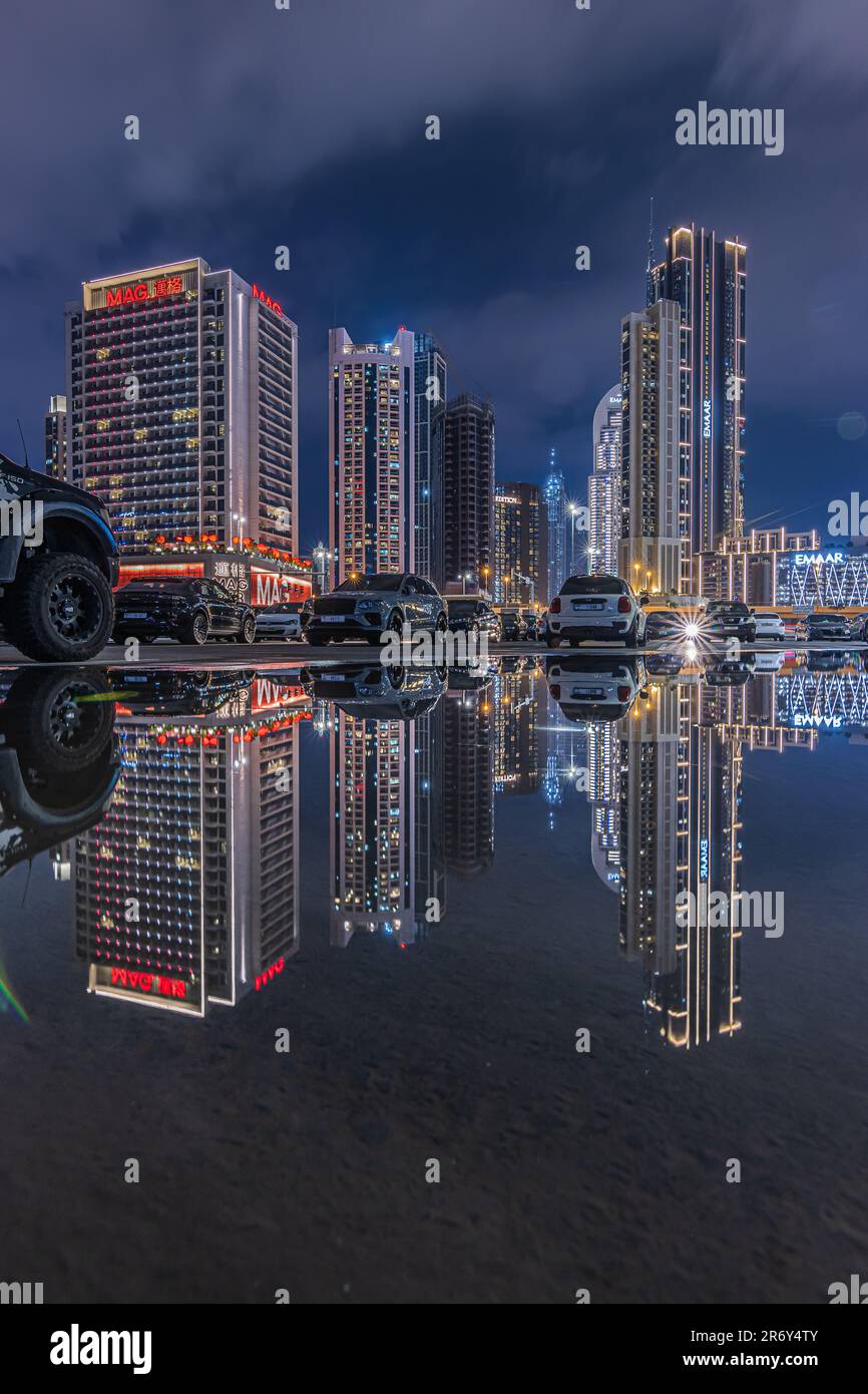 Reflections from skyscrapers and parked cars in Dubai at night time. City of United Arab Emirates at blue hour. Illuminated financial center skyline Stock Photo